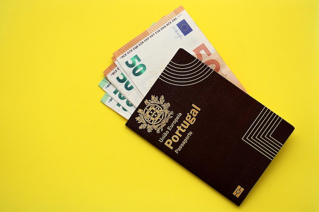 Foto passaporte português vermelho da união europeia e dinheiro em fundo amarelo de perto