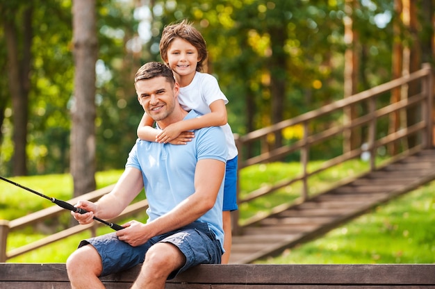 Passar um bom tempo com o pai. Pai e filho felizes pescando juntos e sorrindo enquanto estão sentados no cais