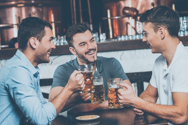 Passar um tempo no bar. Três amigos alegres bebendo cerveja em bar