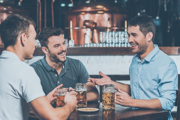 Passar um tempo no bar. três amigos alegres bebendo cerveja em bar