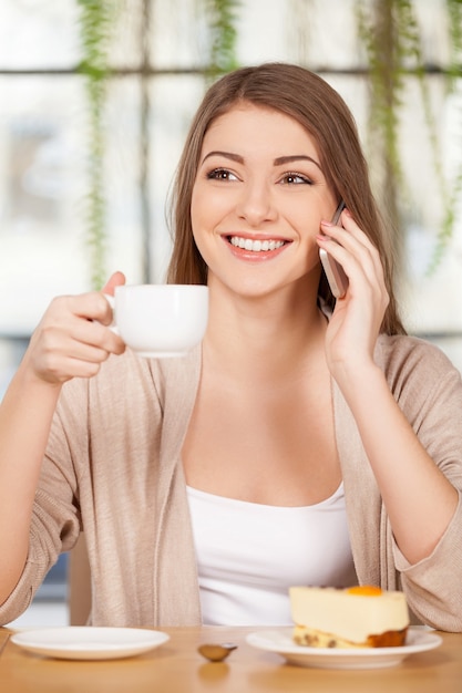 Passar um tempo no restaurante. Mulher jovem e atraente tomando café no restaurante e falando ao telefone