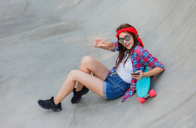 Passatempo da juventude. Mulher jovem hippie descansando com um skate em um skatepark