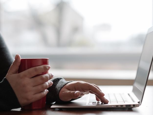 Passatempo de fim de semana ou dia de folga. mulher relaxada sentada perto do laptop do computador e segurando uma xícara. menina lendo as notícias, atualizando o perfil nas redes sociais ou apenas navegando