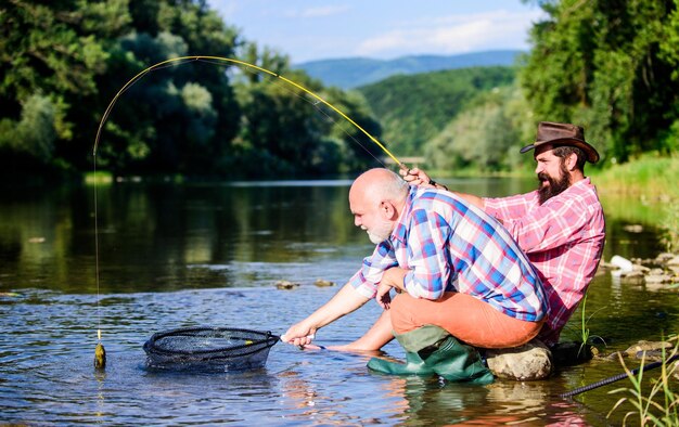 Passatempo de peixe-mosca da pesca de aposentadoria dos homens Dois amigos do sexo masculino pescando juntos pesca de grande porte relaxe na natureza amizade de pescadores felizes pai aposentado e filho barbudo maduro Que peixe