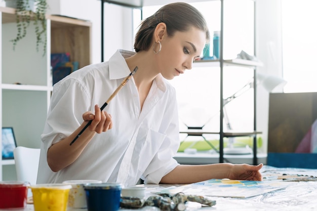 Passatempo de pintura Estilo de vida de artista Lazer criativo em casa Retrato de perfil de mulher pensativa inspirada com tinta acrílica de pincel no estúdio de arte leve