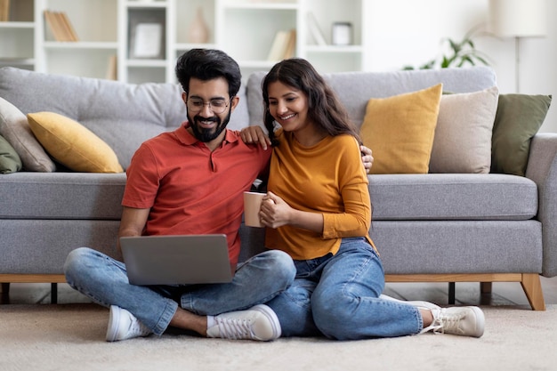 Passatempo doméstico felizes jovens cônjuges indianos descansando com o laptop em casa