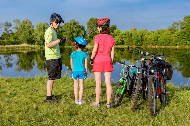 Passeio de bicicleta em família ao ar livre, pais ativos e criança andando de bicicleta e relaxando perto do belo rio