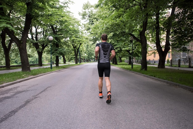 passendes muskulöses männliches Läufertraining für den Marathon, der auf schöne Straße in der Natur läuft.