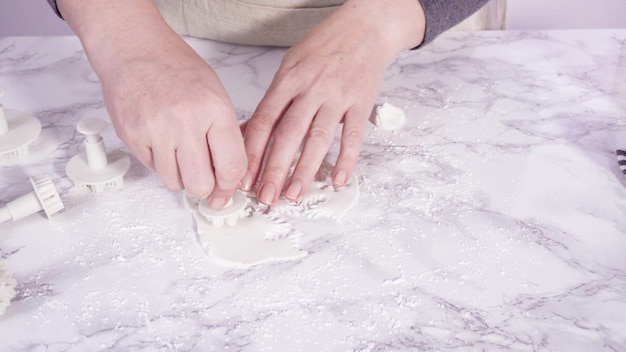 Passo a passo. Cortar flocos de neve com cortadores de biscoito de fondant branco em um balcão de mármore.