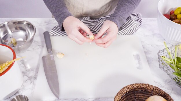 Passo a passo. Cortar legumes em uma tábua branca para fazer uma receita de macarrão de uma panela.