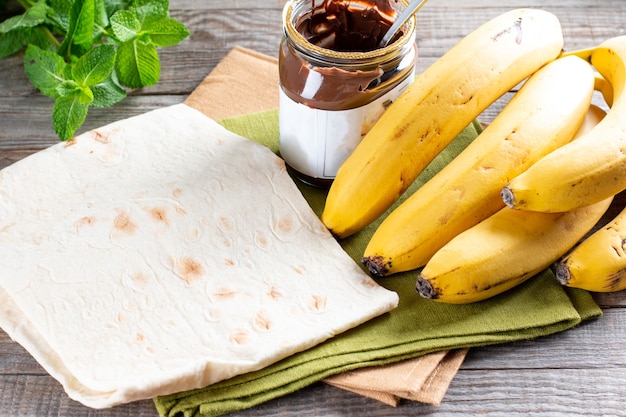 Passo a passo cozinhando um delicioso pãozinho com rodelas de banana na mesa de madeira. Rolinho de banana com sobremesa de chocolate