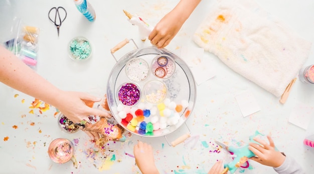 Passo a passo. Meninas decorando unicórnio de papel machê com glitter e flores de papel.