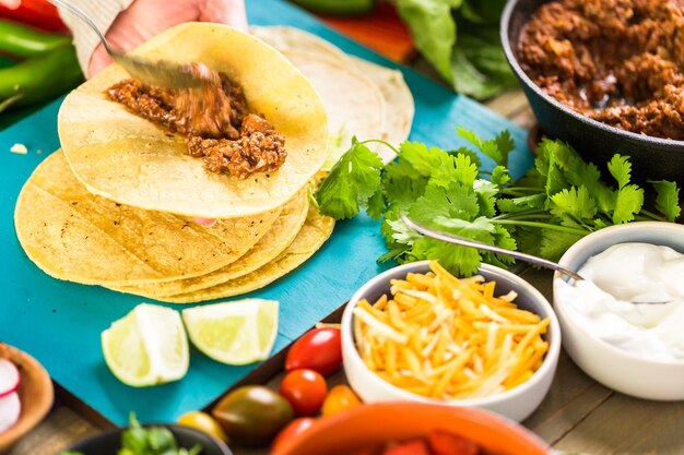 Passo a passo. Tacos de carne moída com alface, tomate picado, rabanete e queijo cheddar ralado.