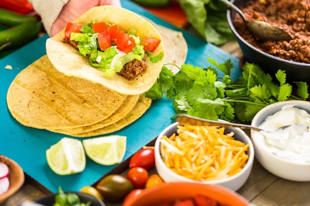 Passo a passo. Tacos de carne moída com alface, tomate picado, rabanete e queijo cheddar ralado.