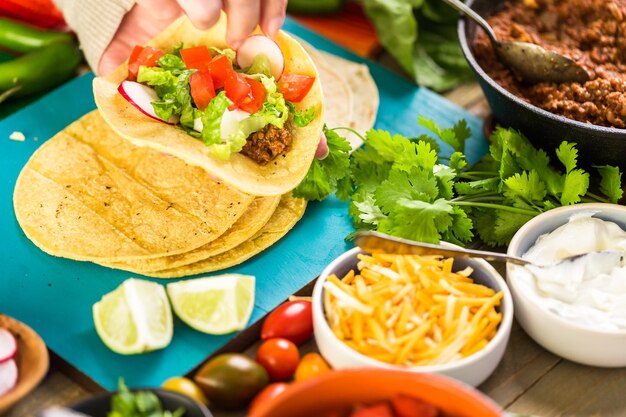 Passo a passo. Tacos de carne moída com alface, tomate picado, rabanete e queijo cheddar ralado.