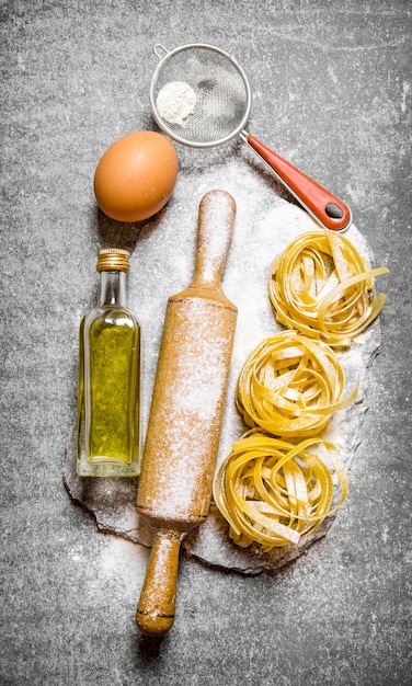 Pasta con aceite de oliva, colador, rodillo y harina sobre soporte de piedra. Sobre la mesa de piedra. Vista superior