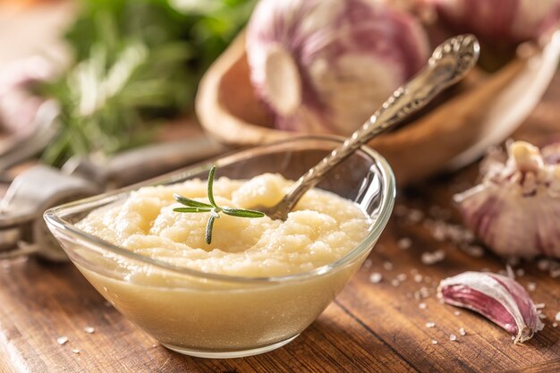 Pasta de ajo en un bol de vidrio con ajo pelado, sal, trituradora y cabezas de ajo.