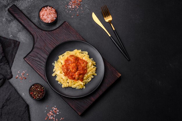 Pasta con albóndigas de ternera en salsa de tomate con especias y hierbas sobre un fondo oscuro