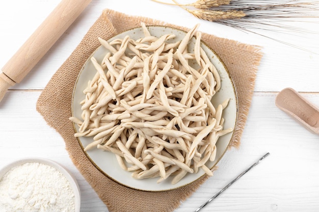 Pasta apuliana cruda de trigo integral llamada Pizzarieddi o maccaruni en un plato de cerámica sobre una mesa de madera blanca