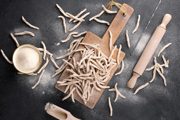 Pasta apuliana de trigo integral Pizzarieddi o maccaruni en una tabla de cortar sobre una mesa negra. Maccheroni fresco plato típico de Puglia, Salento Italia. Fondo de pasta casera italiana, espacio de copia