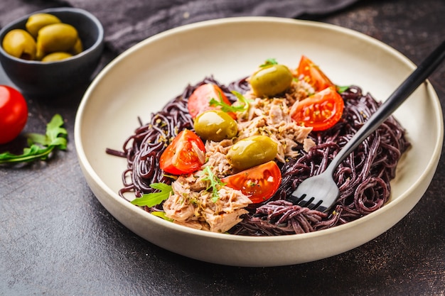 Pasta de arroz negro con atún, tomates y aceitunas en un plato blanco