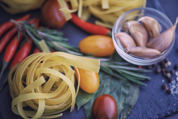 Pasta auf dem Tisch mit Gewürzen und Gemüse. Nudeln mit Gemüse zum Kochen auf schwarzem Steinhintergrund.