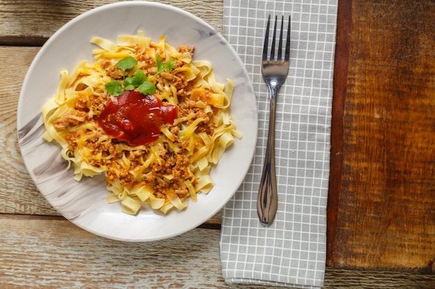 Pasta Bolognese garniert mit Kräutern und Käse in einem Teller auf einem Holztisch neben einer Gabel