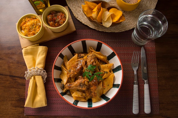 Pasta Bolognese mit Hähnchenflügeln Peru peruanische traditionelle Hausmannskost mise en place Holztisch