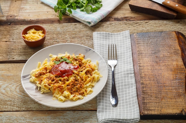 Pasta boloñesa aderezada con hierbas y queso en un plato sobre una mesa de madera sobre un soporte