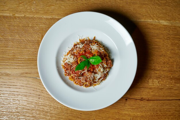 Pasta boloñesa con carne picada, queso y salsa de tomate en un plato blanco sobre mesa de madera. Vista superior de comida. cocina italiana