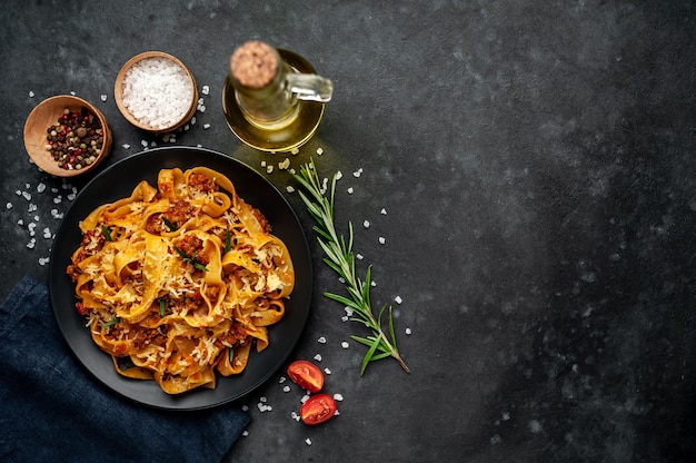 Foto pasta boloñesa con especias, plato de pasta italiana con carne picada y tomates en un plato oscuro sobre un fondo de piedra