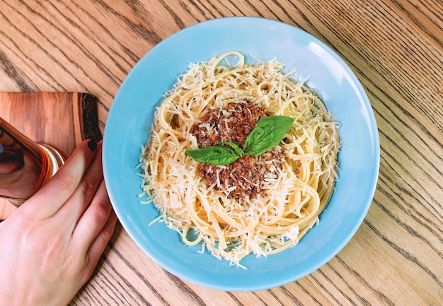 pasta boloñesa en el plato y mano sosteniendo cerveza oscura en la mesa del bar