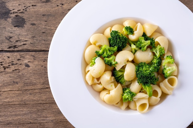 Pasta con brócoli en un plato blanco y una mesa de madera