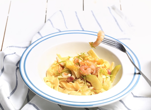 Pasta con calabacín y mariscos en un plato blanco con un tenedor sobre un paño de cocina sobre fondo blanco.