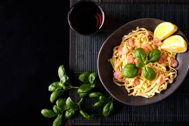 Pasta con camarones, albahaca y tomates sobre un fondo oscuro. Vista desde arriba