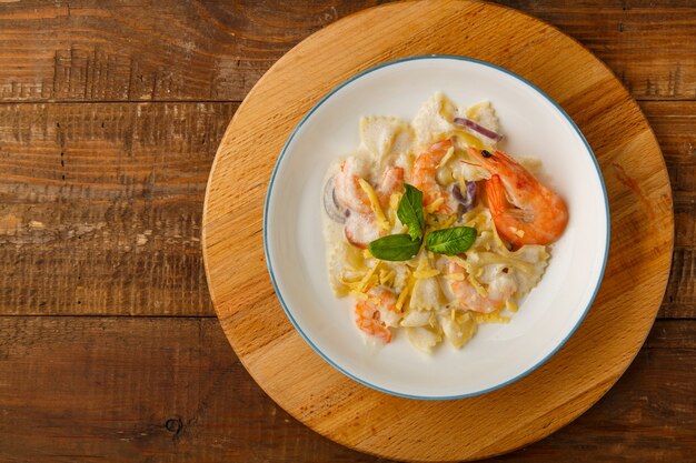 Pasta con camarones en salsa cremosa decorada con espinacas sobre una placa gris sobre una mesa de madera sobre un pedestal.