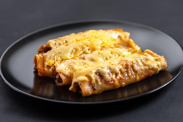 Pasta de canelones de carne caliente sobre mesa de madera y fondo negro