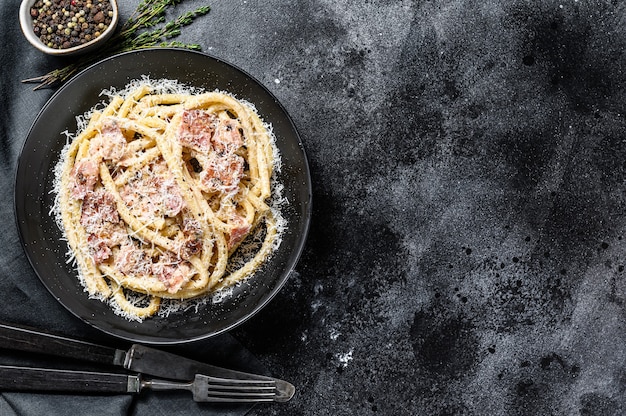 Pasta carbonara, bucatini con panceta, huevo, queso parmesano y salsa de crema. Fondo negro