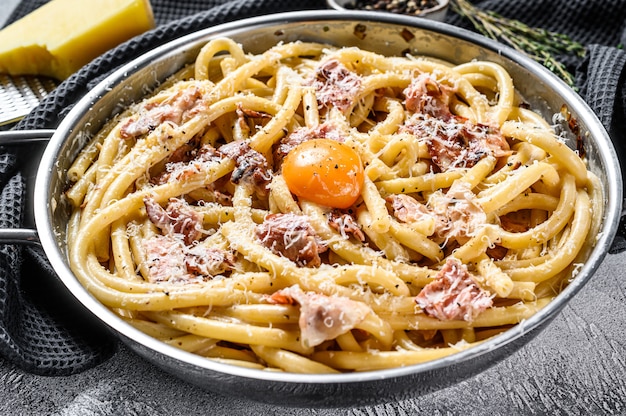 Pasta Carbonara, bucatini en la sartén. Fondo gris