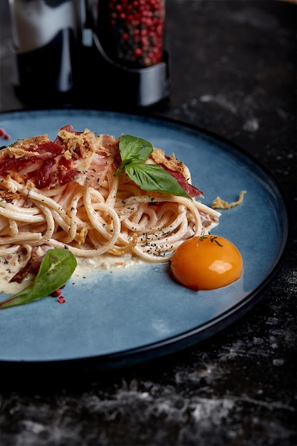 Pasta carbonara clásica con yema en un plato Pasta dispuesta en un plato azul sobre un fondo oscuro Concepto de cocina italiana hermosos platos para servir primer plano