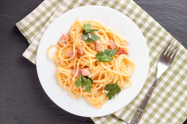 Pasta carbonara con jamón y queso sobre toalla cuadriculada. Vista superior.