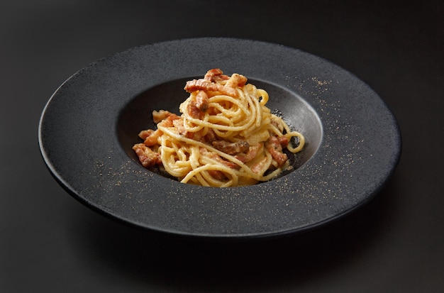 Pasta Carbonara mit Speck in einer schwarzen Platte isoliert auf schwarzem Hintergrund