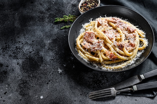 Pasta a la carbonara en placa negra con parmesano, bucatini. Vista superior. Copia espacio