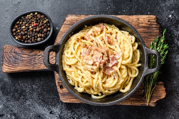 Foto pasta carbonara con tocino y parmesano en una sartén. fondo negro. vista superior.