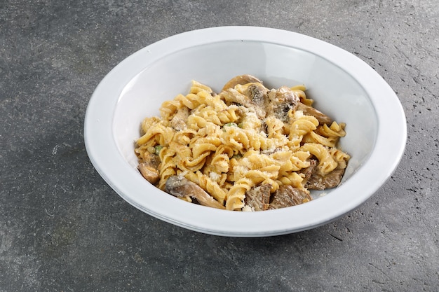 Pasta con champiñones en plato blanco sobre espacio de copia de fondo de hormigón