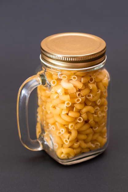 Pasta chifferi rigati cruda en frasco de vidrio sobre fondo negro