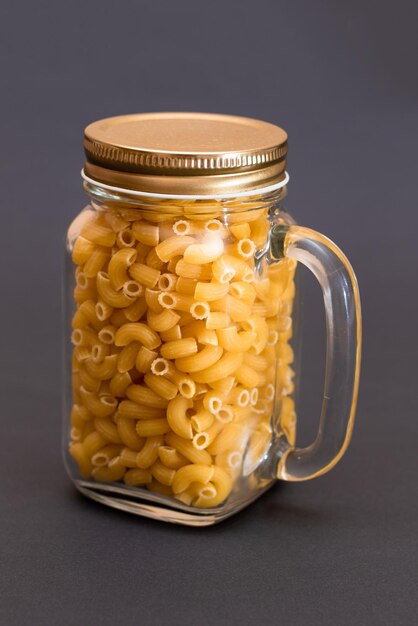 Pasta chifferi rigati cruda en frasco de vidrio sobre fondo negro