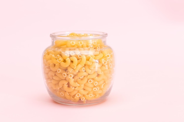 Pasta chifferi rigati cruda en frasco de vidrio sobre fondo rosa