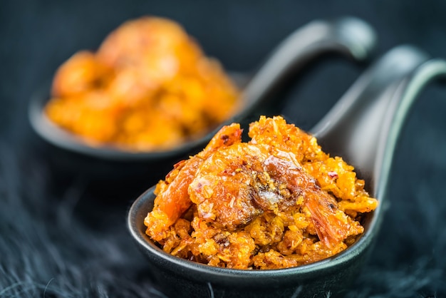 Pasta de chile con camarones crujientes picantes en cuchara negra sobre pared oscura