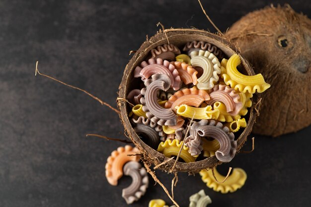 Pasta de colores en forma de vieiras artesanales en un plato de coco sobre una pared gris vintage, vista superior